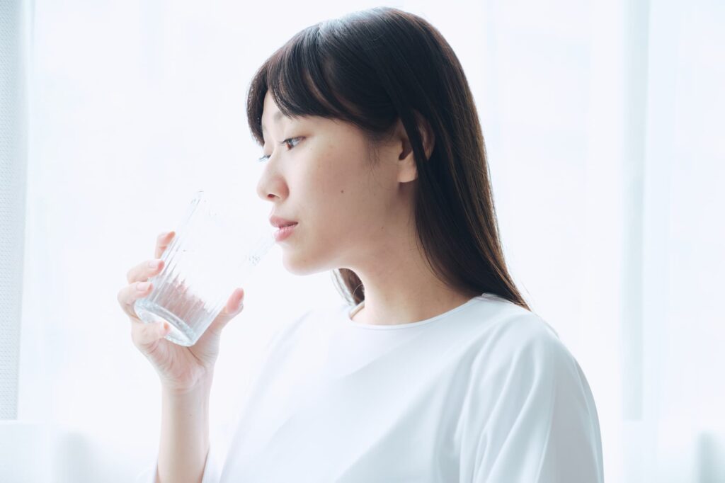 窓のそばで水を飲む女性
